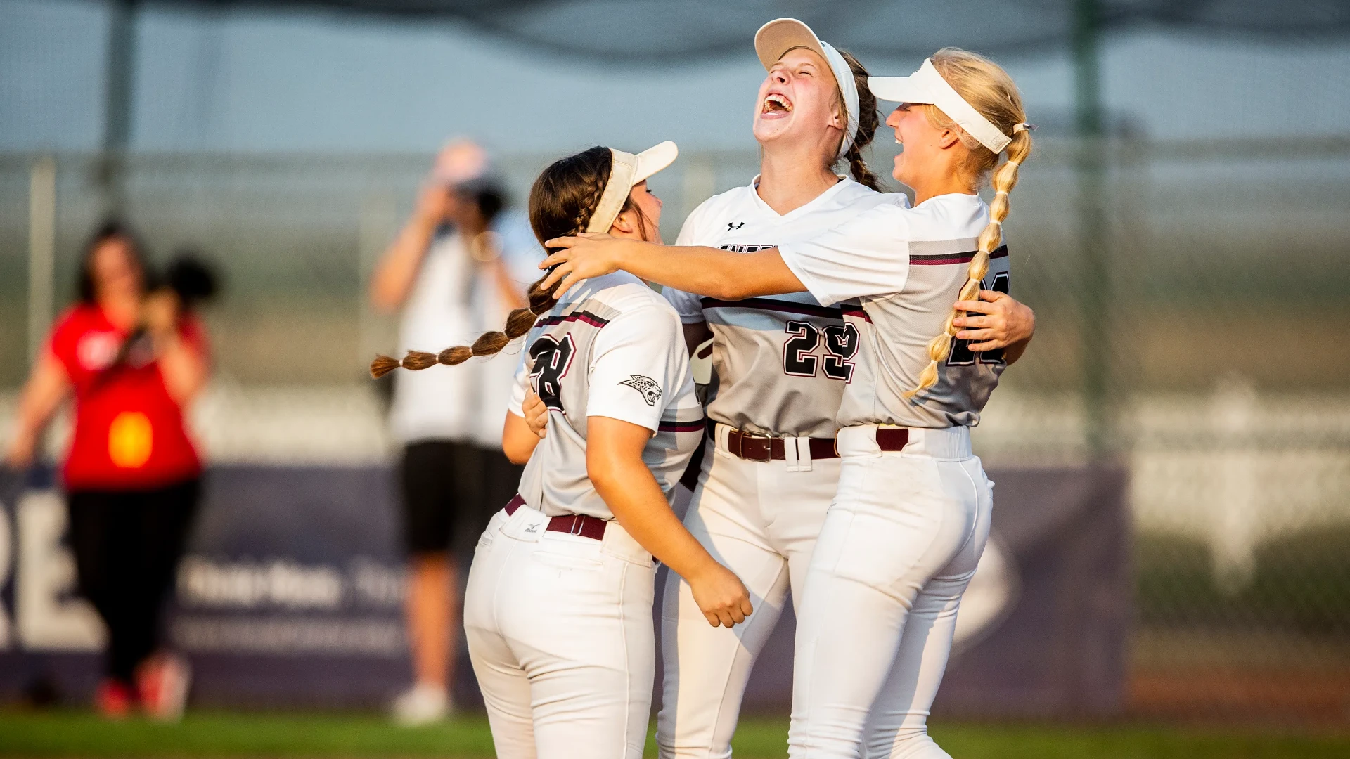 Three softball players in uniform hugging and laughing on the field after a win